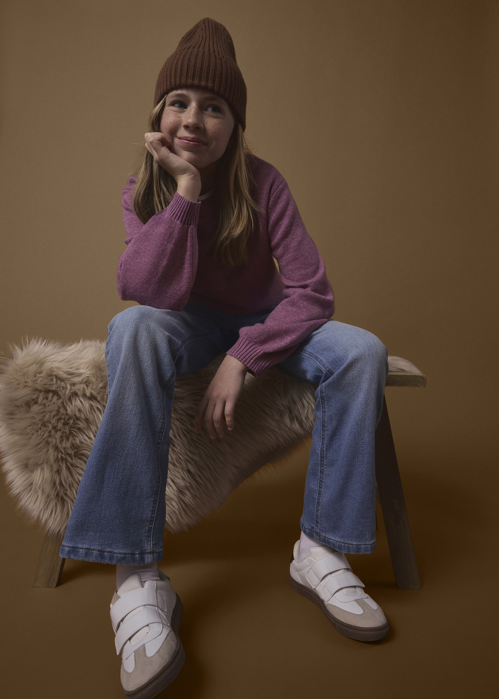 Strickmütze, rosa Pullover, weite Jeans und moderne Sneaker bilden ein lässiges Outfit.