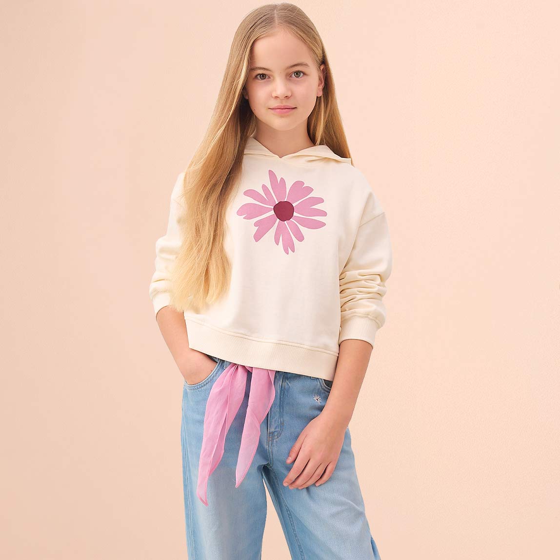 Helles Sweatshirt mit Blumenaufdruck, hellblaue Jeans mit rosa Gürtel. 