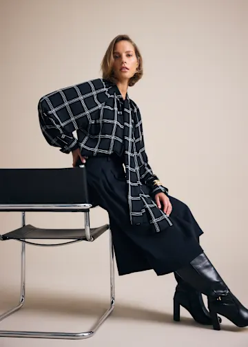 Stilvolles Outfit: Karierte Bluse, weite Hose und kniehohe Lederstiefel.