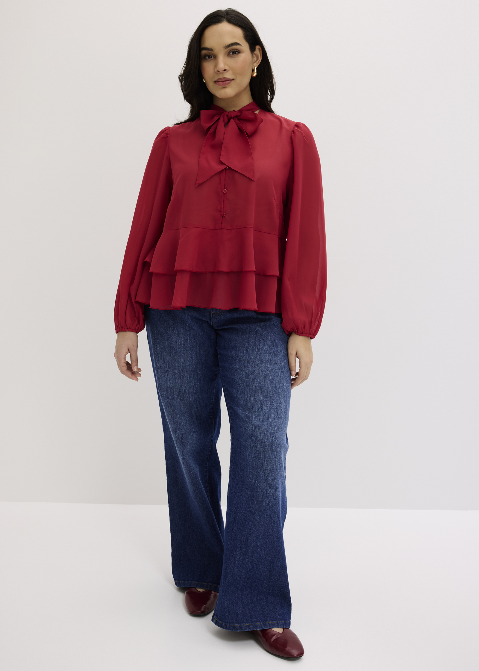 Rote Bluse mit Schleifenkragen und Rüschen, kombiniert mit weiten Jeans und roten Schuhen.