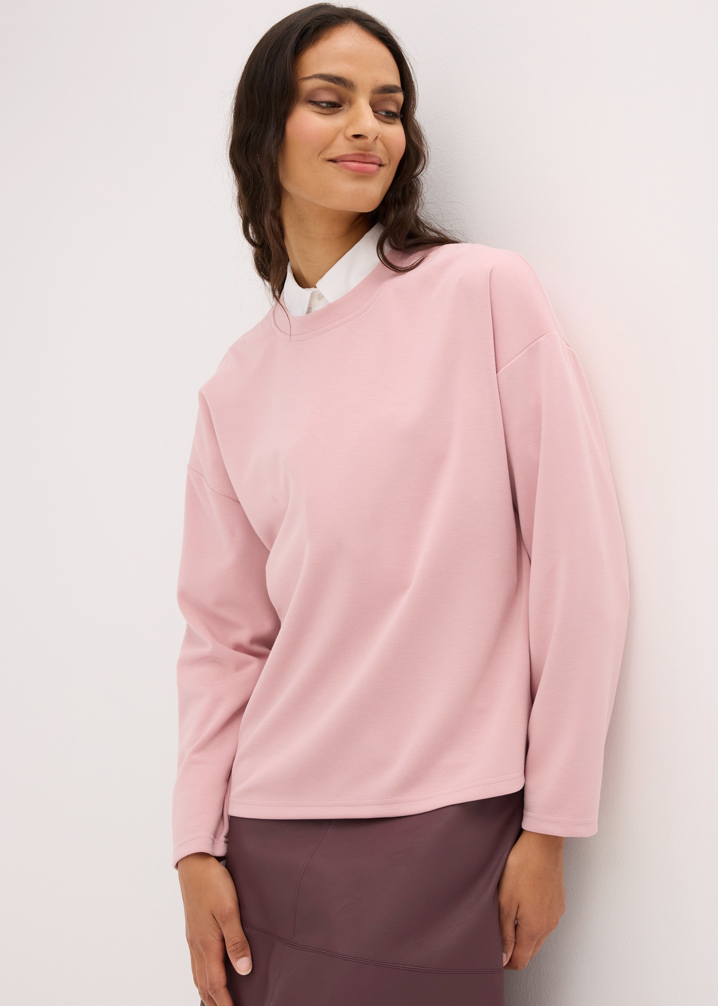 Rosa Oversize-Sweatshirt über weißem Hemd, dazu ein eleganter dunkler Rock.