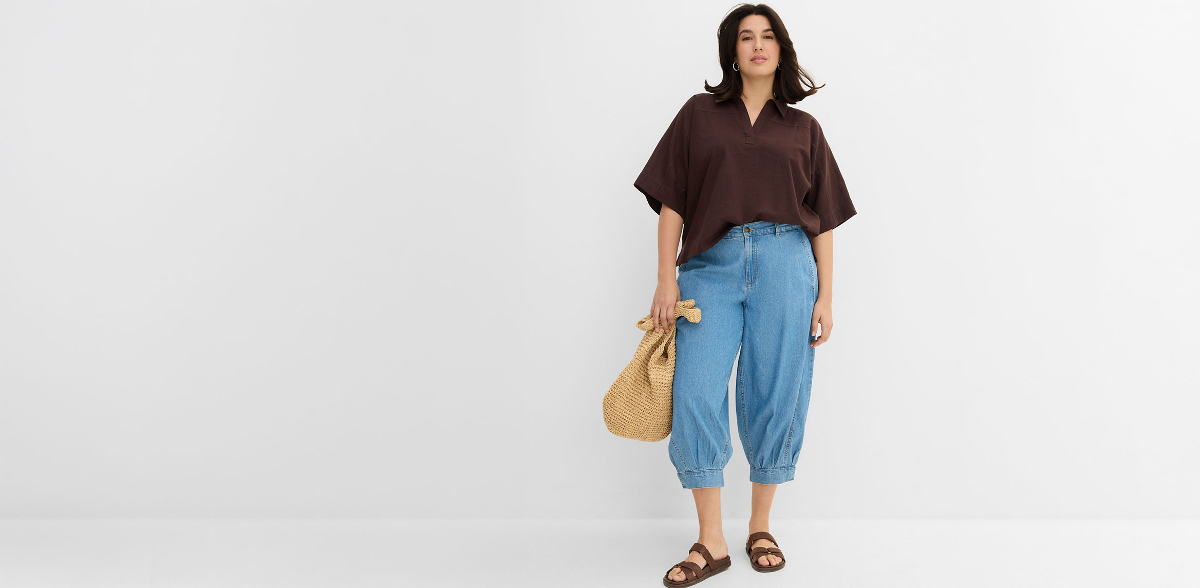 Kombination aus brauner Bluse und weiter Jeans mit Sandalen und Strohtasche.