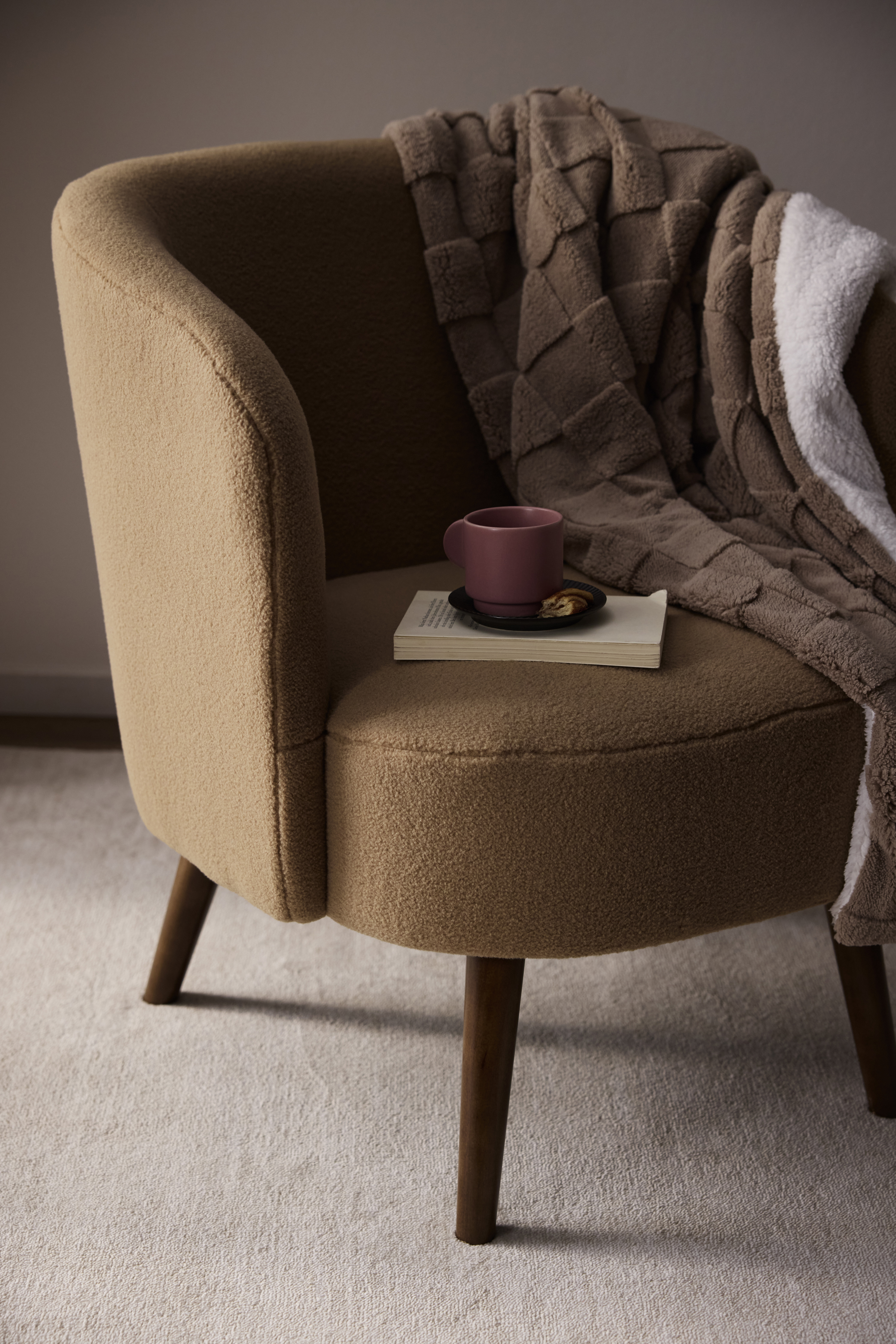 Gemütlicher Sessel mit brauner Decke, Buch und Tasse.