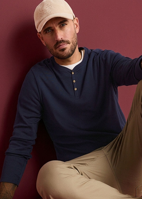 Der Mann trägt eine beige Kappe, ein marineblaues Henley-Shirt und beige Hosen.