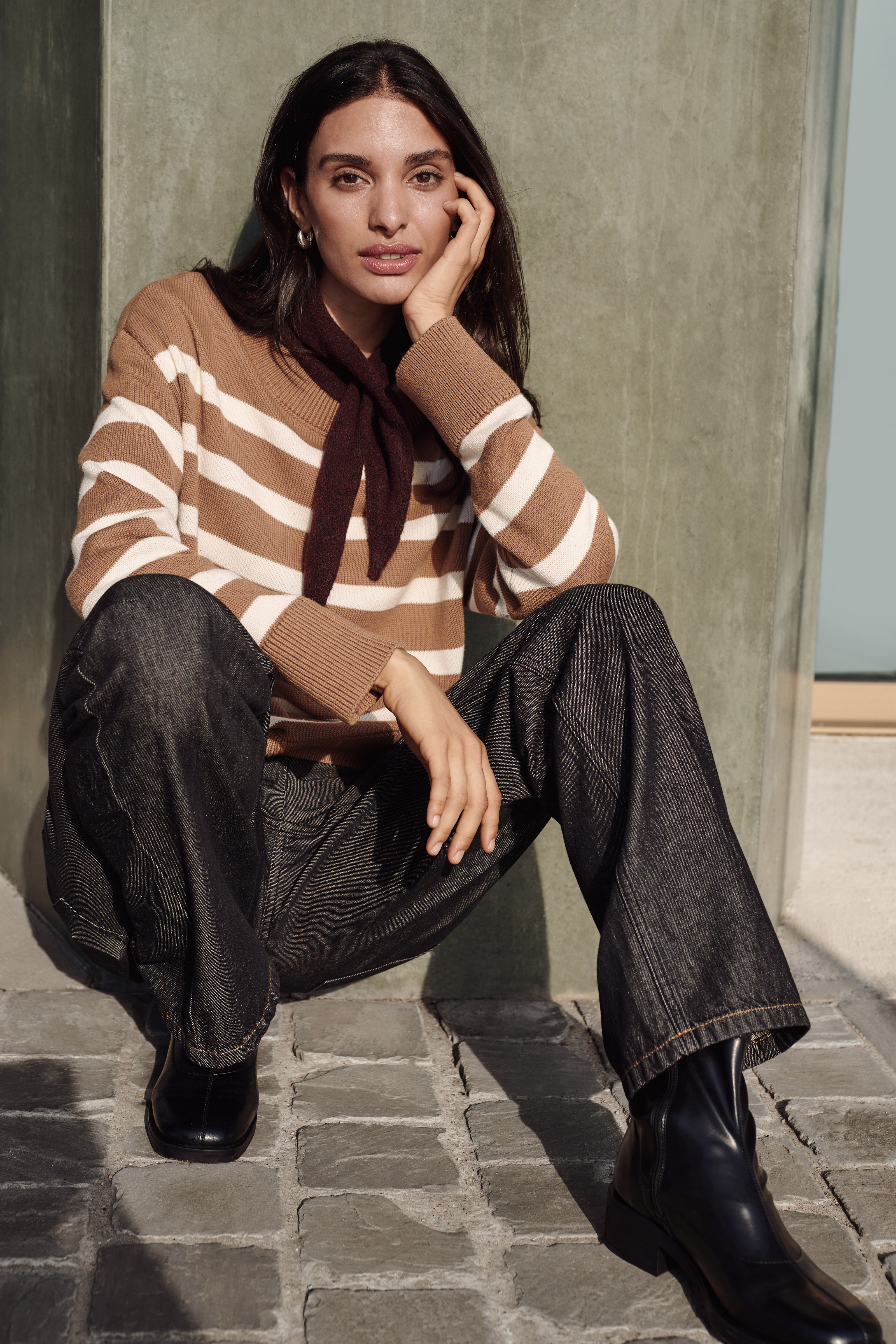 Lässig in gestreiftem Pullover, gemusterter Hose, dunklem Schal und schwarzen Stiefeletten.