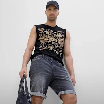 Mann trägt schwarze Kappe, ärmelloses Top mit Golddruck und lässige Jeans-Shorts.