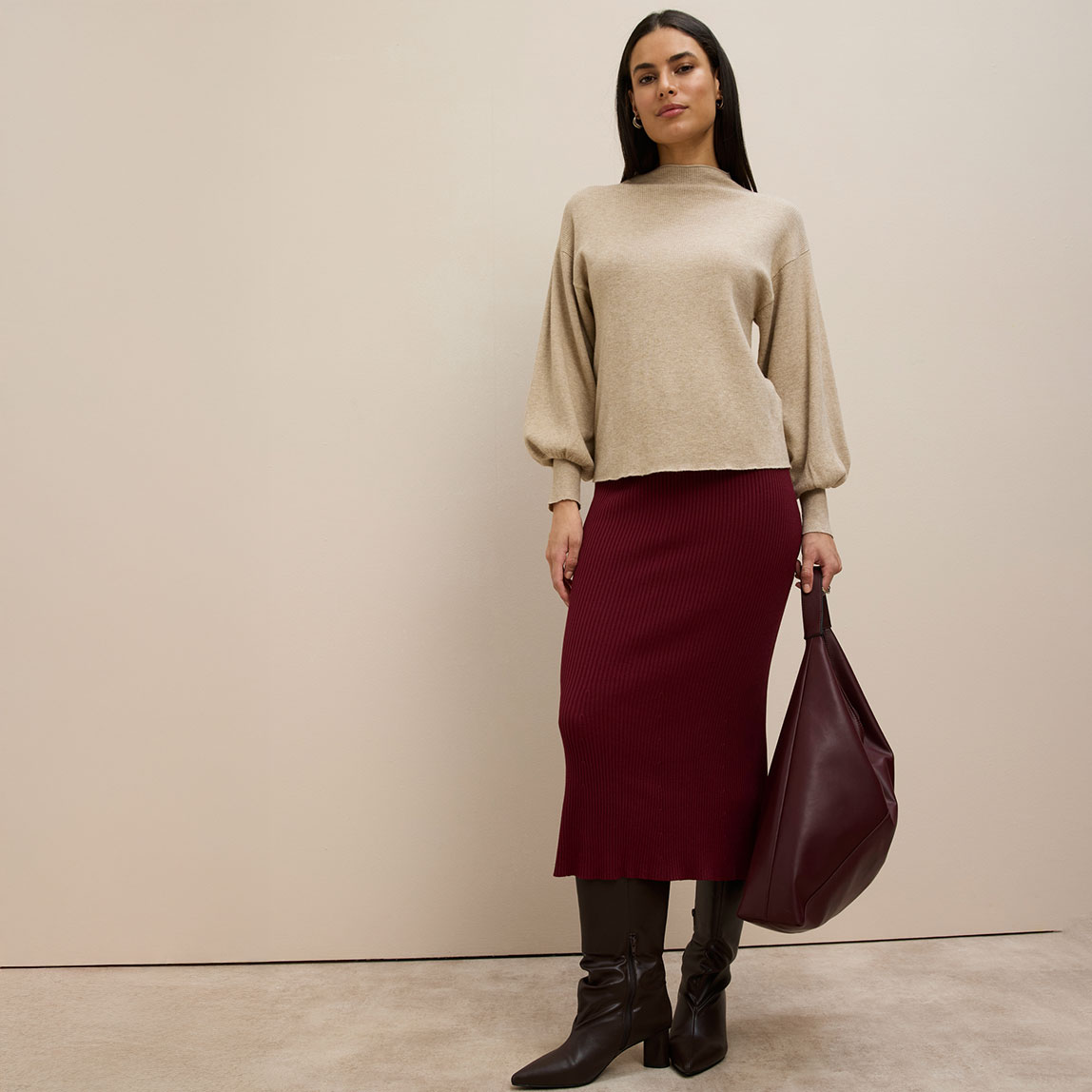 Beiger Pullover, weinroter Strickrock, braune Stiefel und große bordeauxfarbene Handtasche.