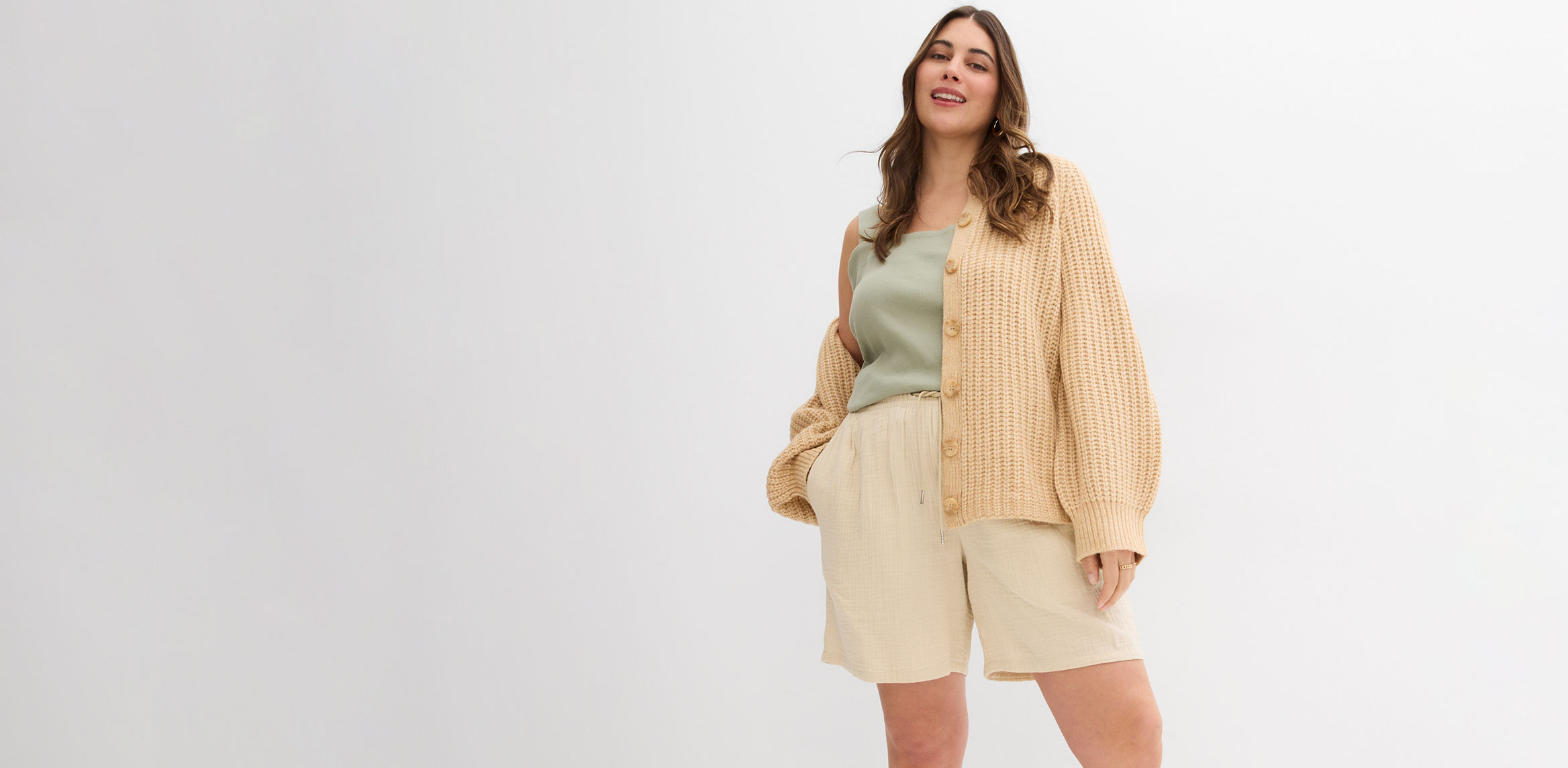 Frau trägt beigen Cardigan, hellgrünes Top und cremefarbene Shorts.