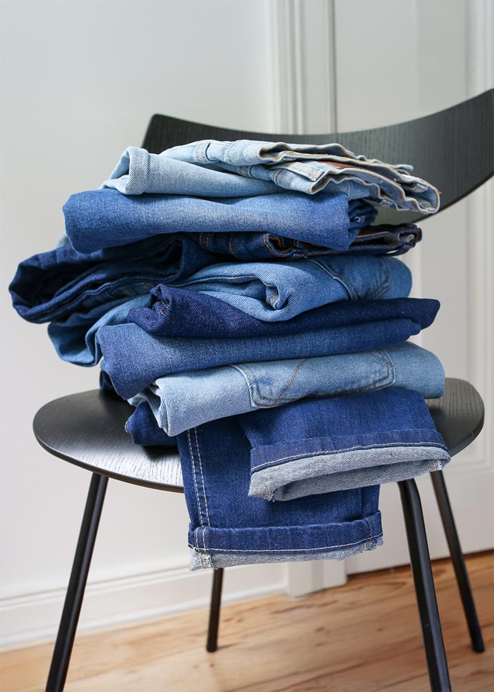 Ein Stapel verschiedener Jeans in unterschiedlichen Blautönen liegt ordentlich gefaltet auf einem Stuhl.