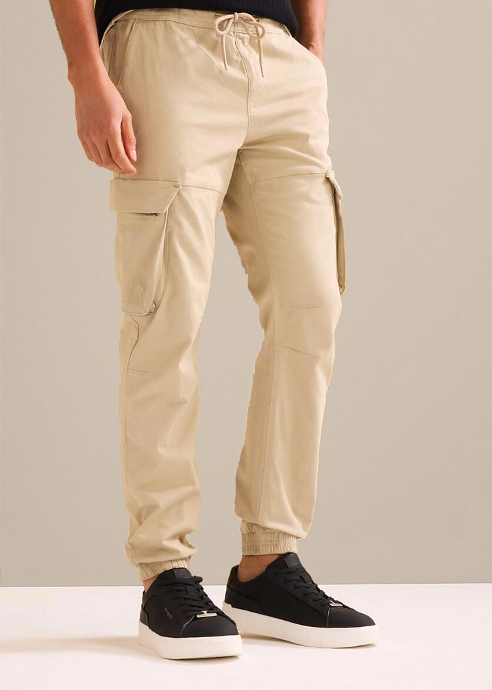Bequeme beige Cargohose mit Seitentaschen, kombiniert mit schwarzen Sneakern.