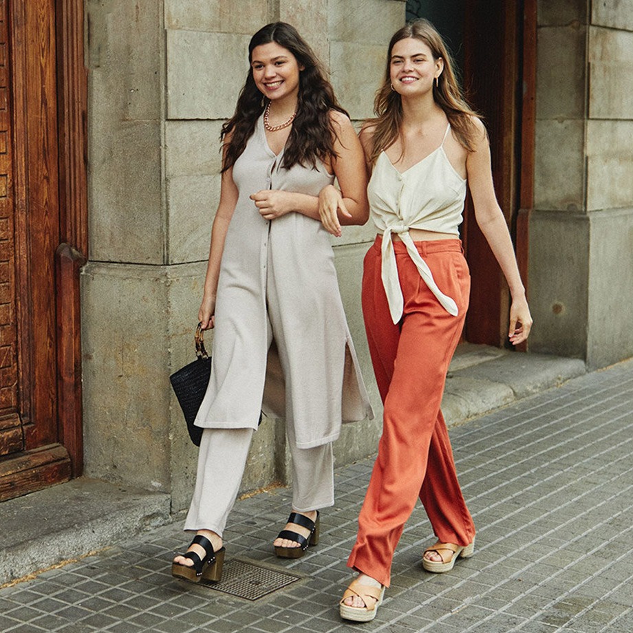Sommerliche Eleganz: Helle Hosenanzüge und fließende Tops, kombiniert mit orangefarbener Hose und Espadrilles.