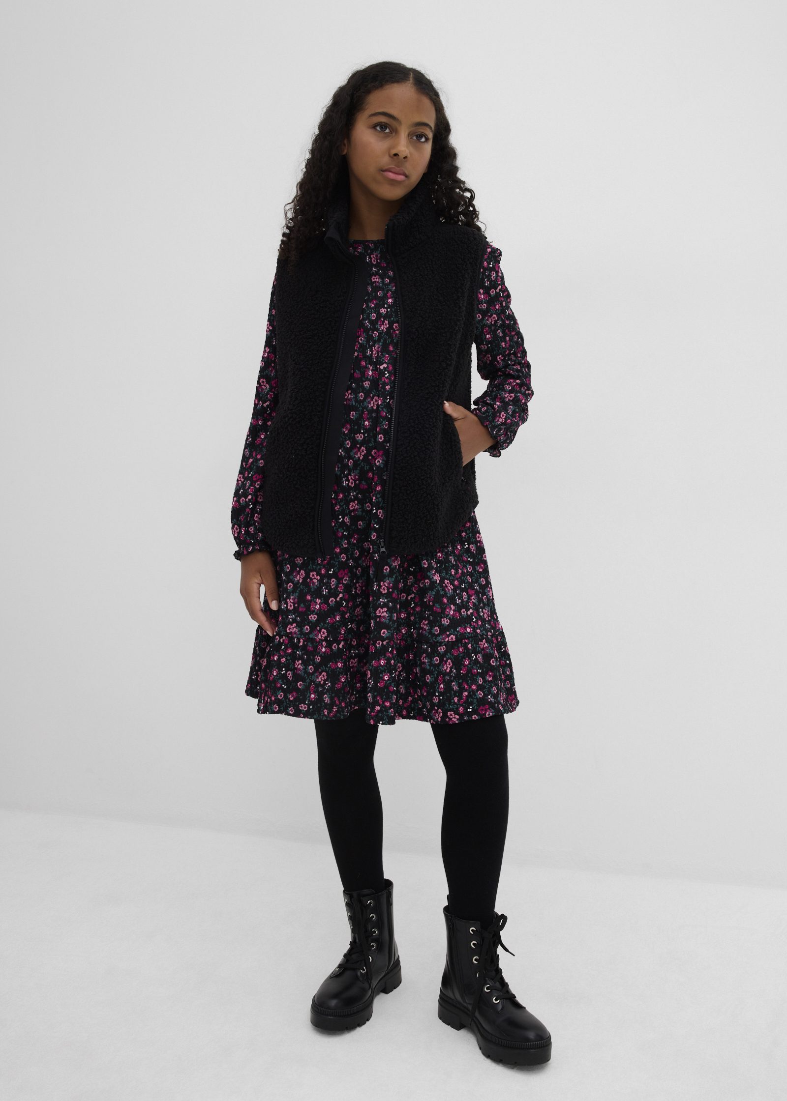 Schwarze Teddy-Weste über geblümtem Kleid.