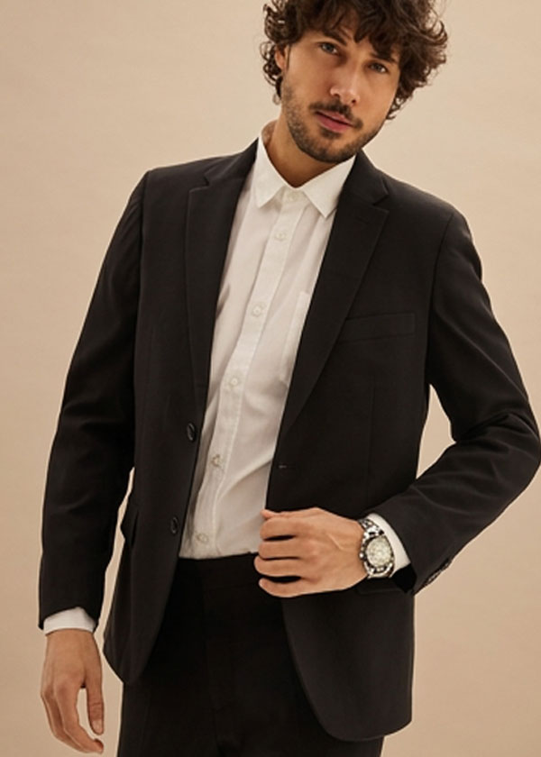 Mann trägt eleganten schwarzen Anzug mit weißem Hemd und modischer Armbanduhr.