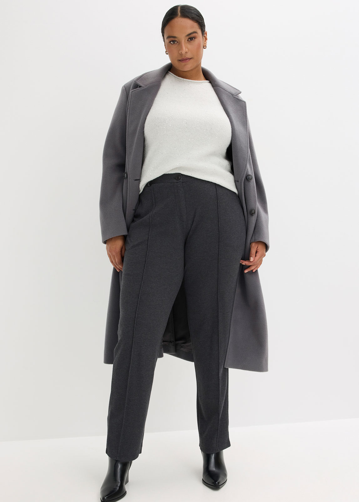 Grauer Mantel über weißem Pullover und dunkler Hose.