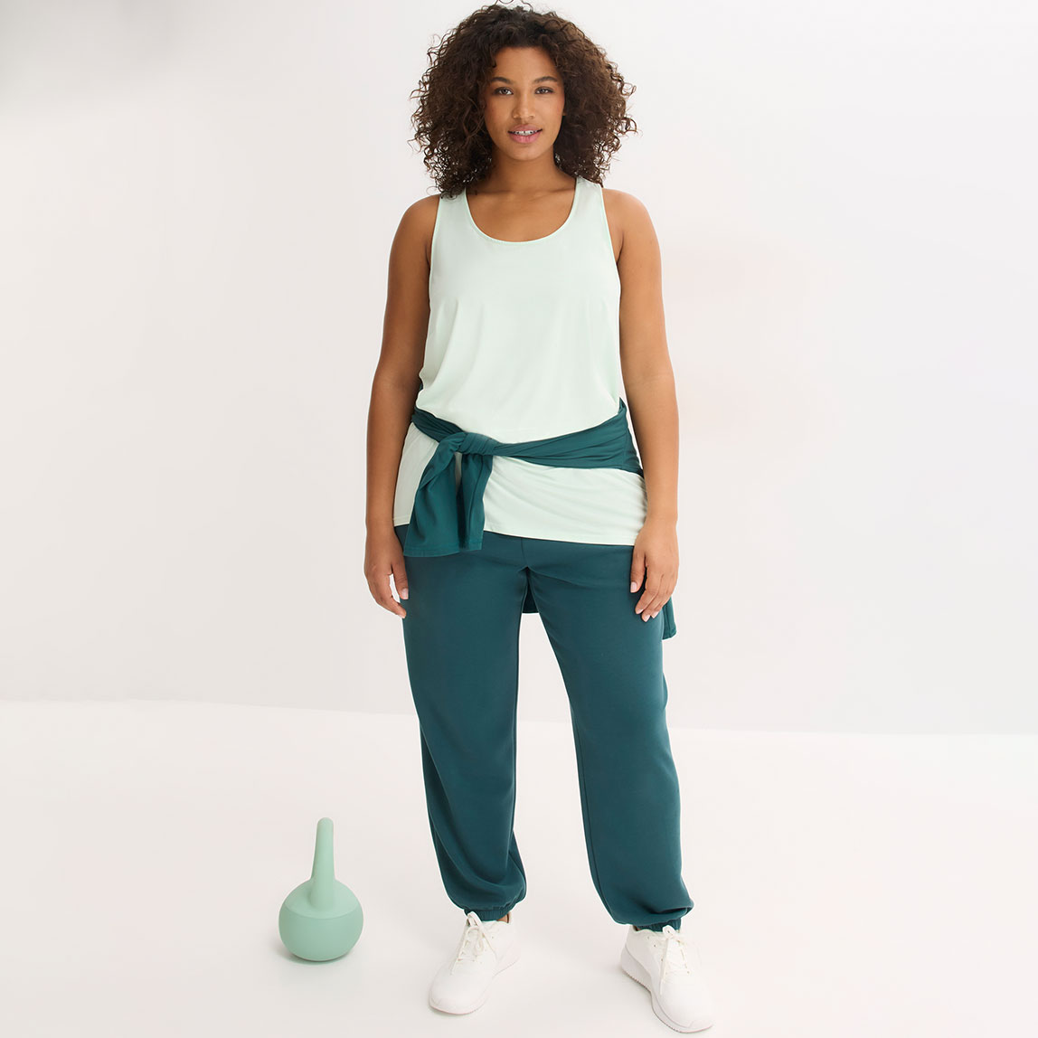 Mintfarbenes Sportshirt, grüne Jogginghose und weißen Sneakers.