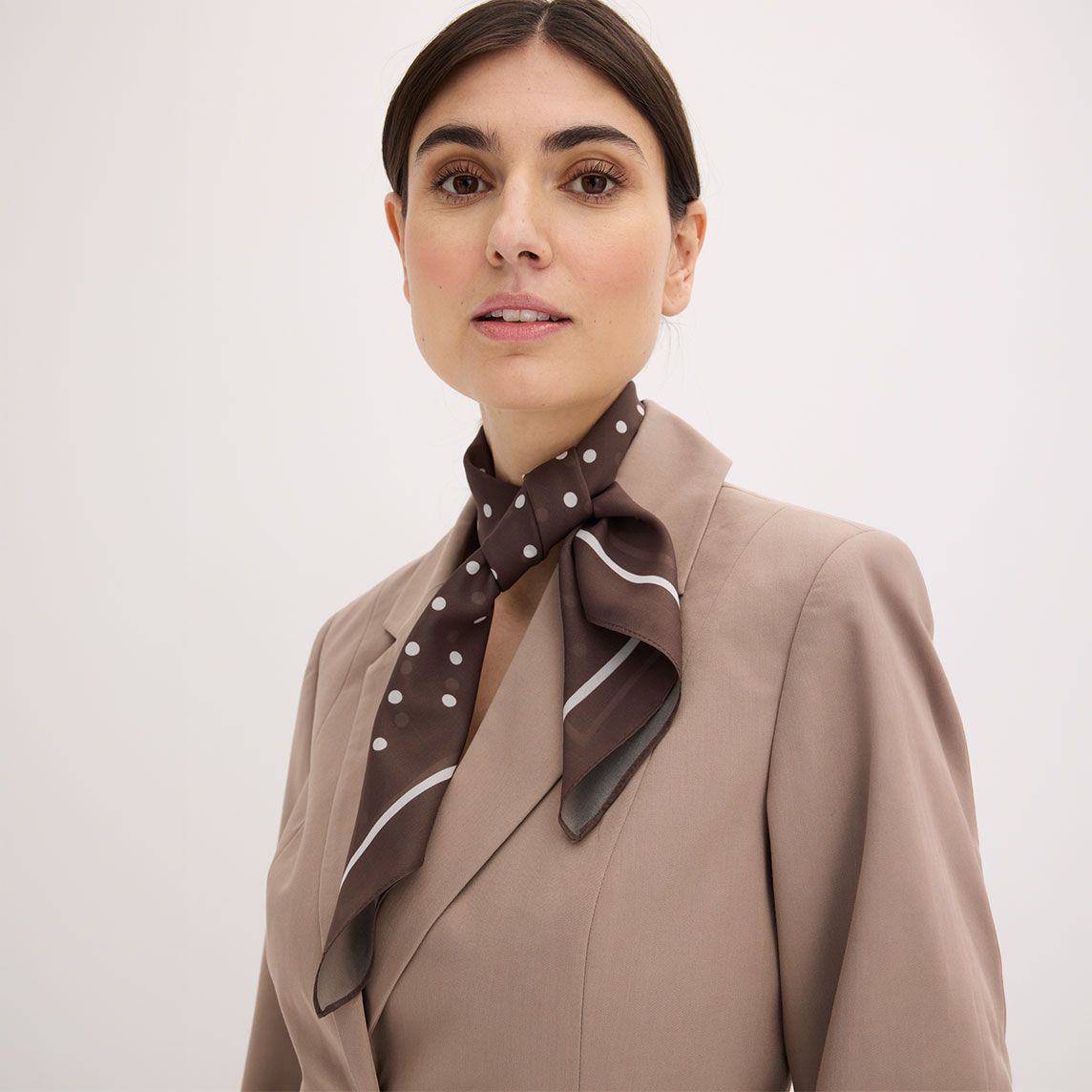 Eleganter beiger Blazer kombiniert mit einem gepunkteten braunen Halstuch für stilvolle Businesslooks.