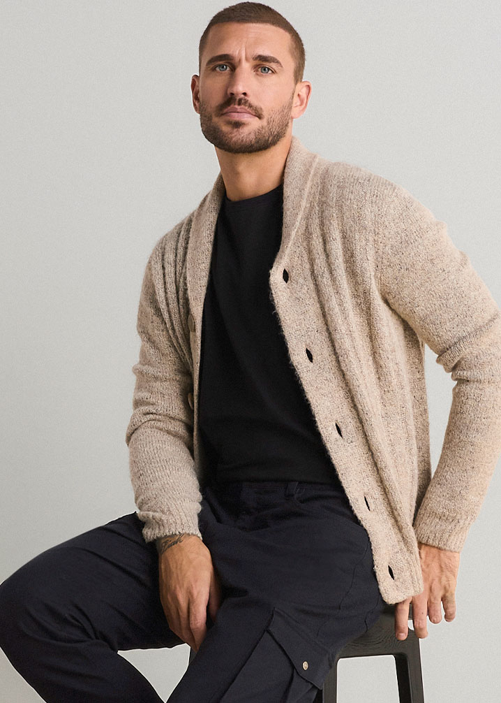 Lässiger Look: beige Strickjacke, schwarzes T-Shirt und dunkelblaue Cargohose.