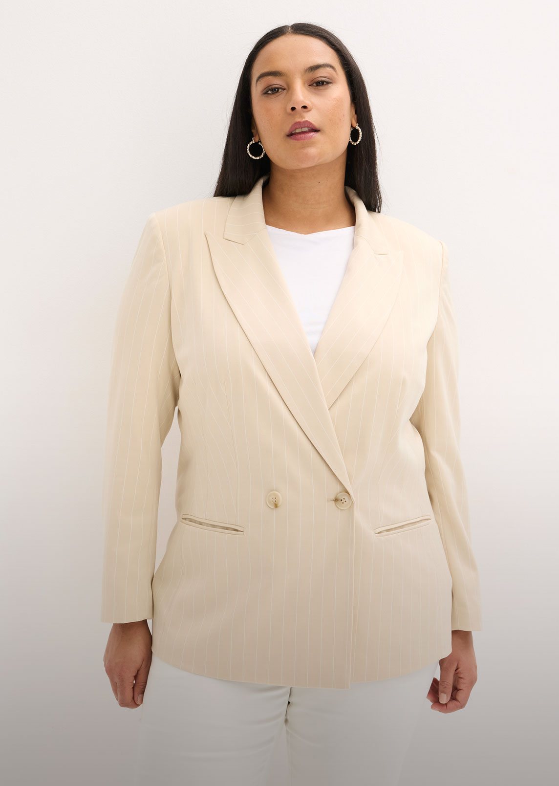 Eleganter beigefarbener Nadelstreifen-Blazer über weißem Top, kombiniert mit weißer Hose.