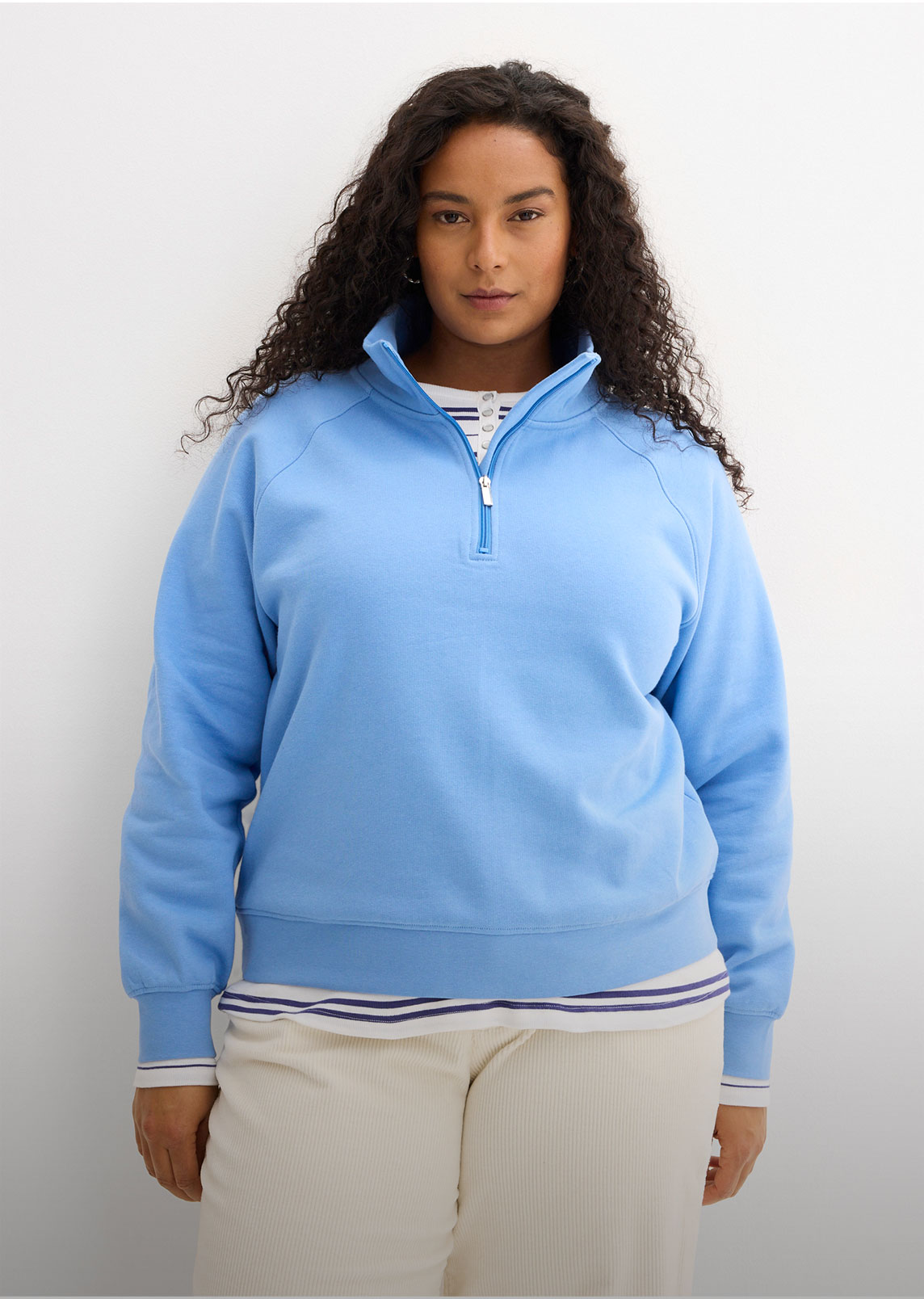 Hellblaues Sweatshirt mit Reißverschluss, gestreiftes Shirt und bequeme helle Hose.