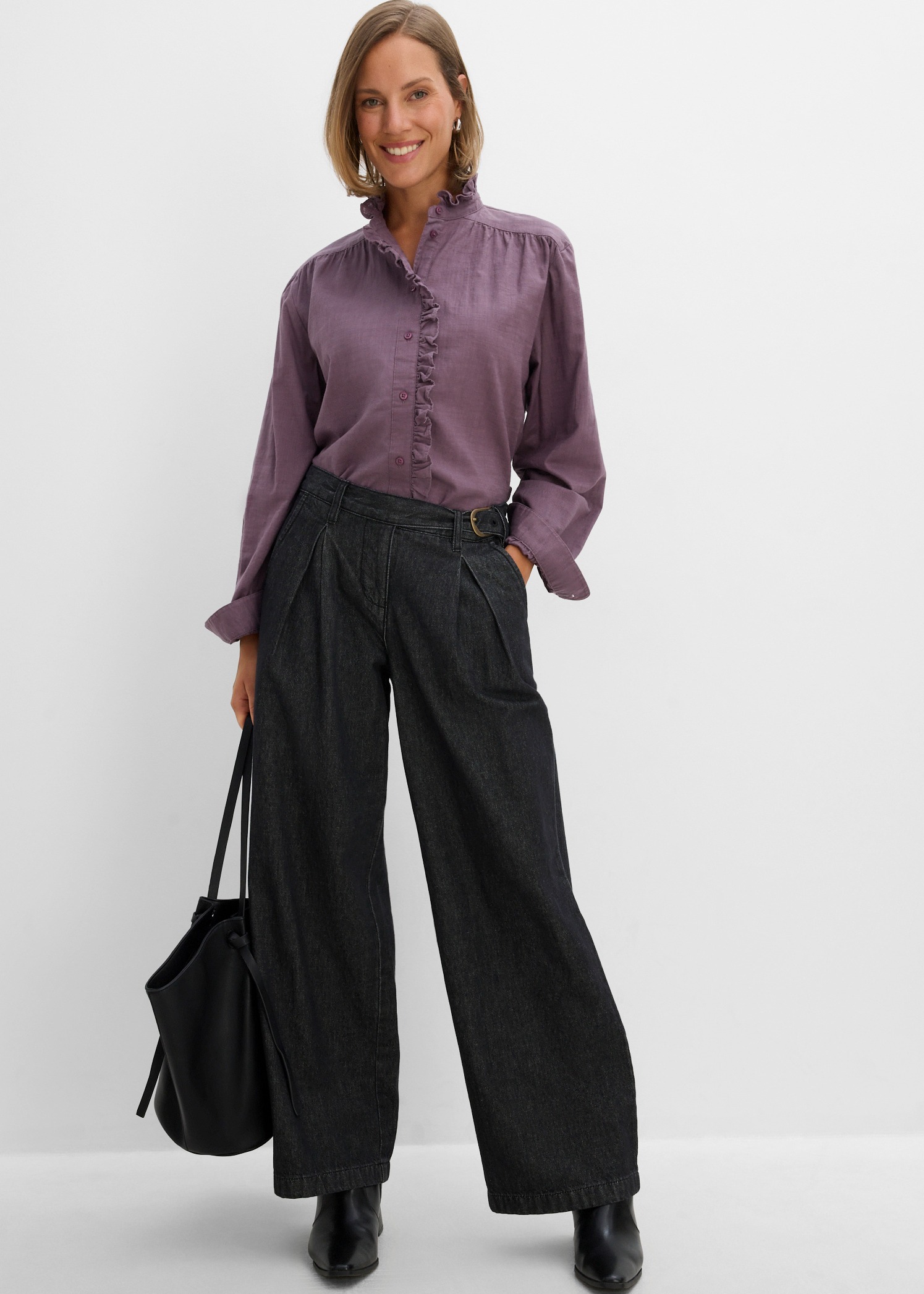 Schicke lila Rüschenbluse mit weiten, dunklen Jeans, dazu schwarze Stiefeletten und Shopper.