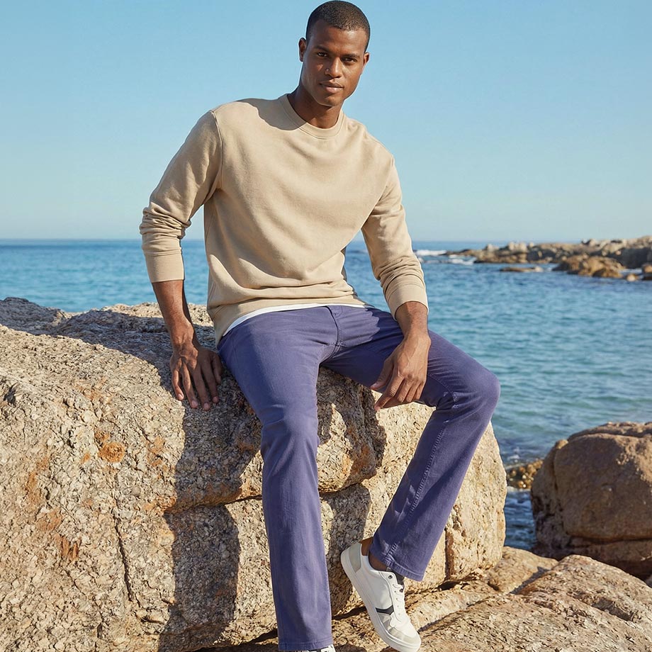 Beiger Pullover und lila Hose harmonieren perfekt mit der Meereskulisse.