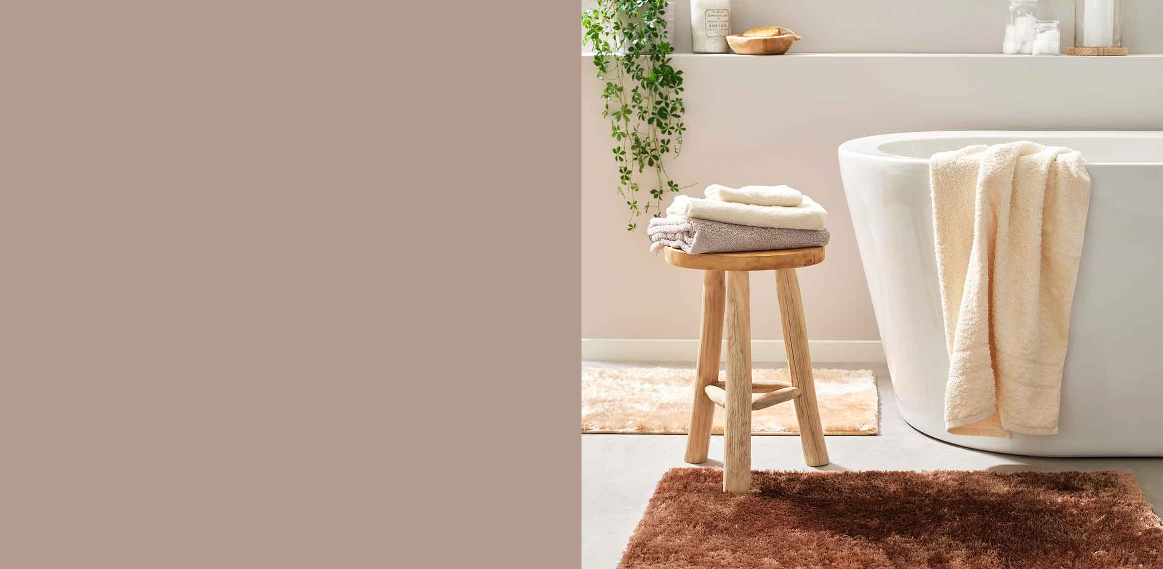 Helle Handtücher auf Holzhocker neben Badewanne. Warme Farben und natürliche Materialien im Badezimmer.