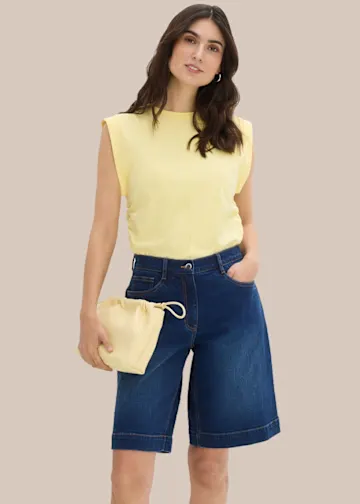 Gelbes Top mit Schulterpolstern, blaue Jeans-Bermuda und passende Beuteltasche.