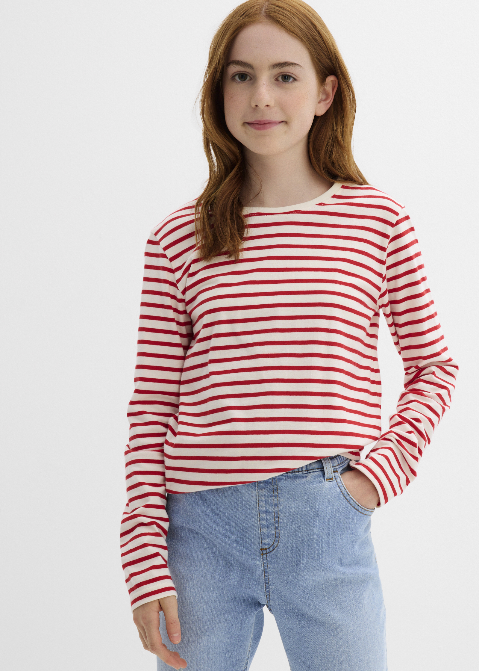 Sie trägt ein rot-weiß gestreiftes Langarmshirt und eine helle Jeans.