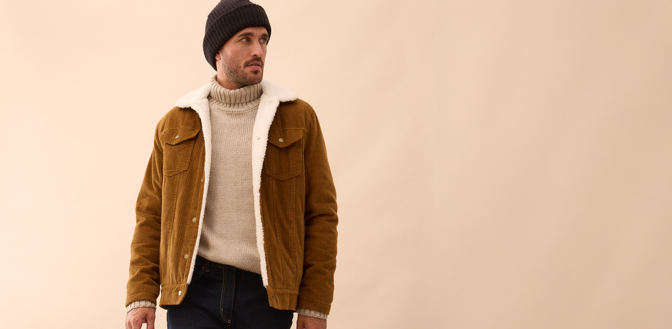 Stilvolle Kombination aus brauner Wildlederjacke, cremefarbenem Rollkragenpullover und schwarzer Mütze.