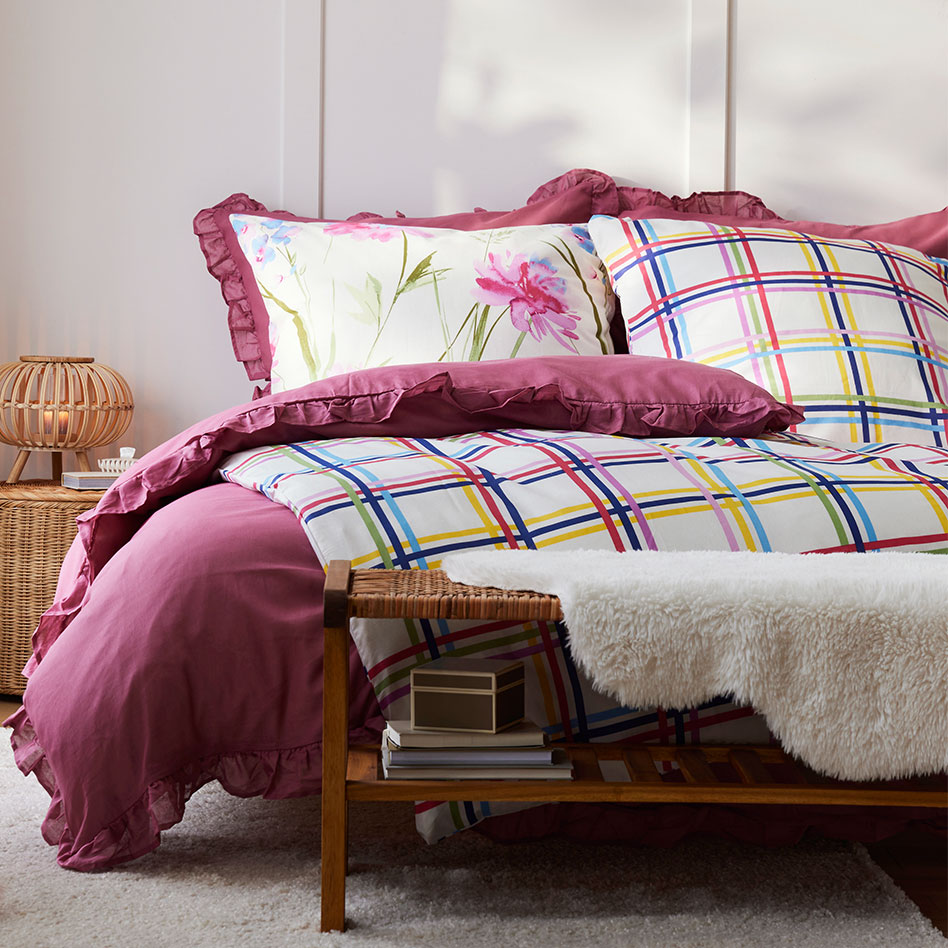 Farbenfrohe Bettwäsche mit Blumenmuster und Karos. Gemütliche Decke und Kissen in warmen Tönen.