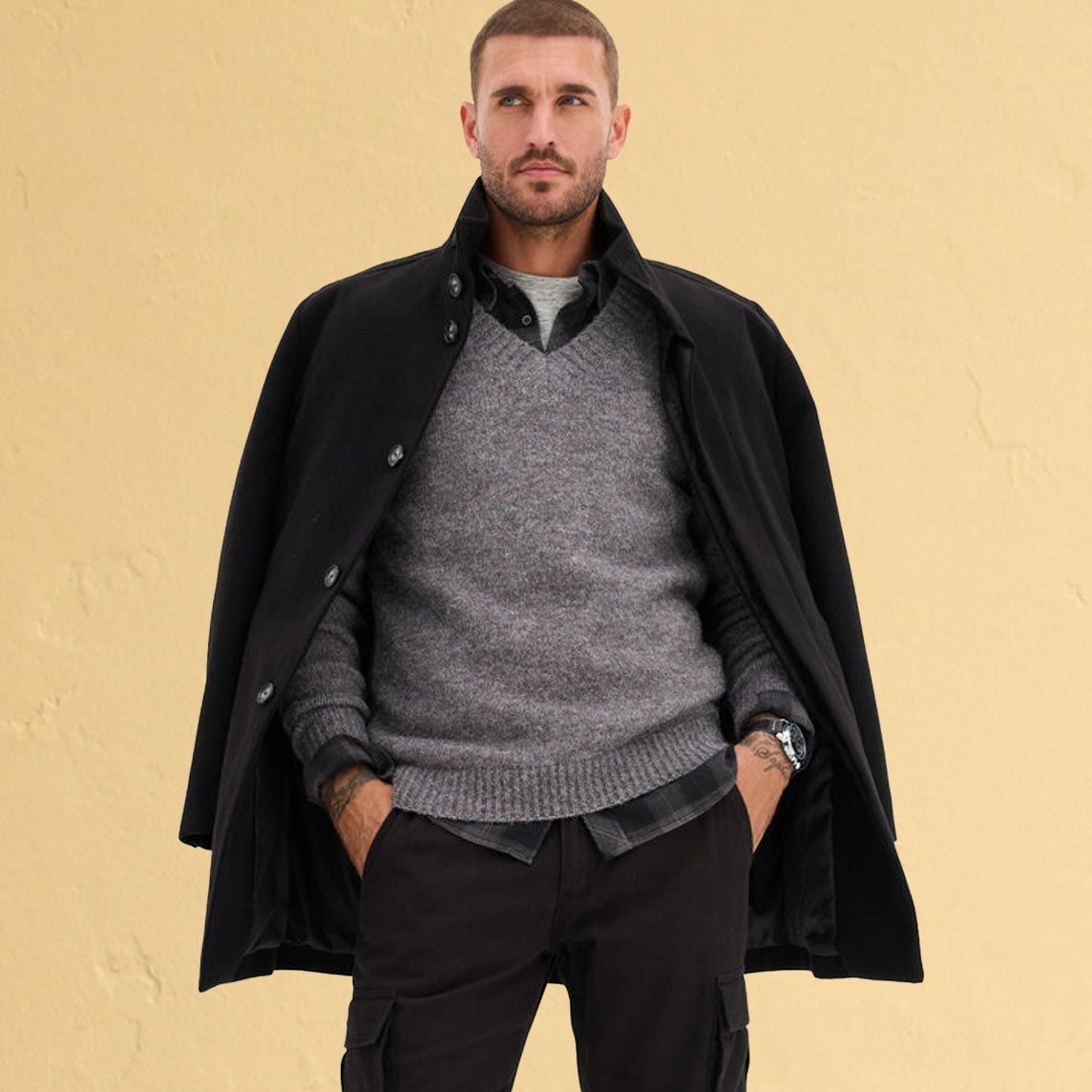 Eleganter, schwarzer Mantel, grauer Pullover und dunkler Hose. 