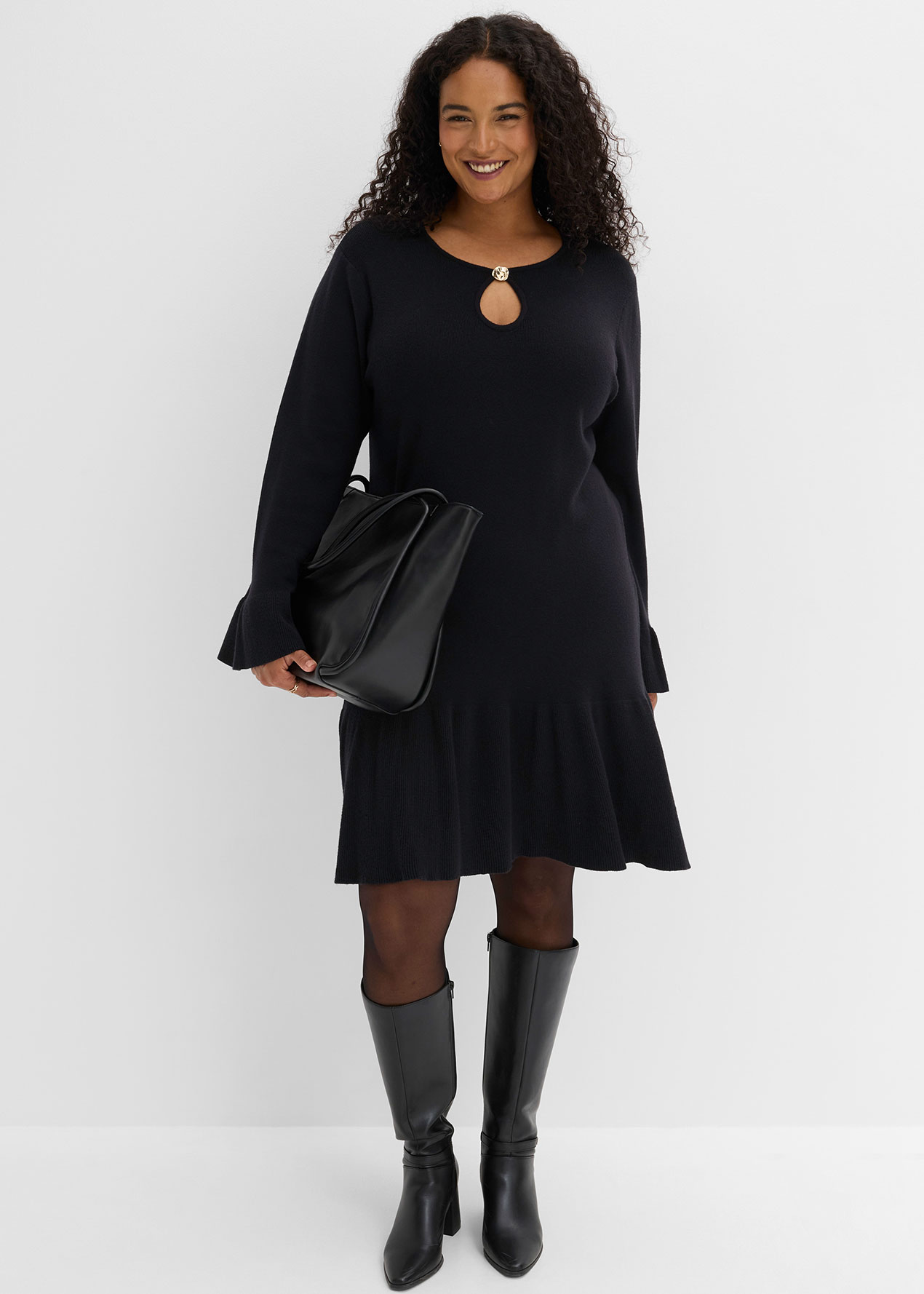 Elegantes schwarzes Kleid mit Ausschnitt, dazu Strumpfhose, kniehohe Stiefel und Handtasche.