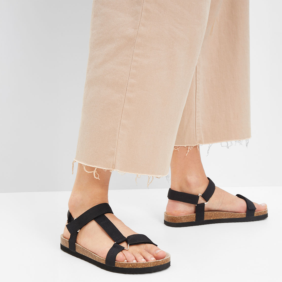 Schwarze Sandalen mit Riemen ergänzen die beige weite Hose perfekt für einen lässigen Look.