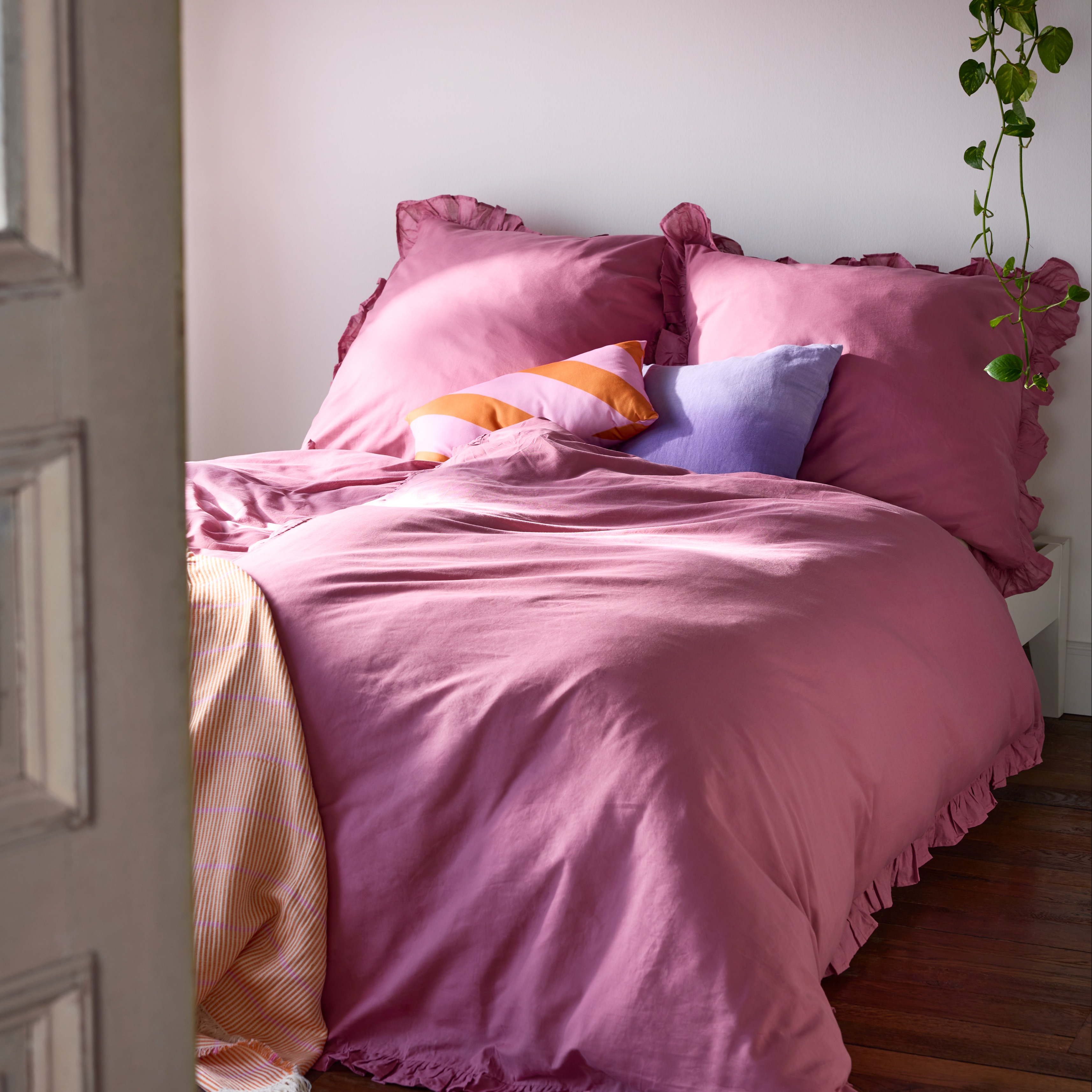 Rosa Bettwäsche mit Rüschen ziert das Bett, ergänzt durch bunte Kissen und Decken.