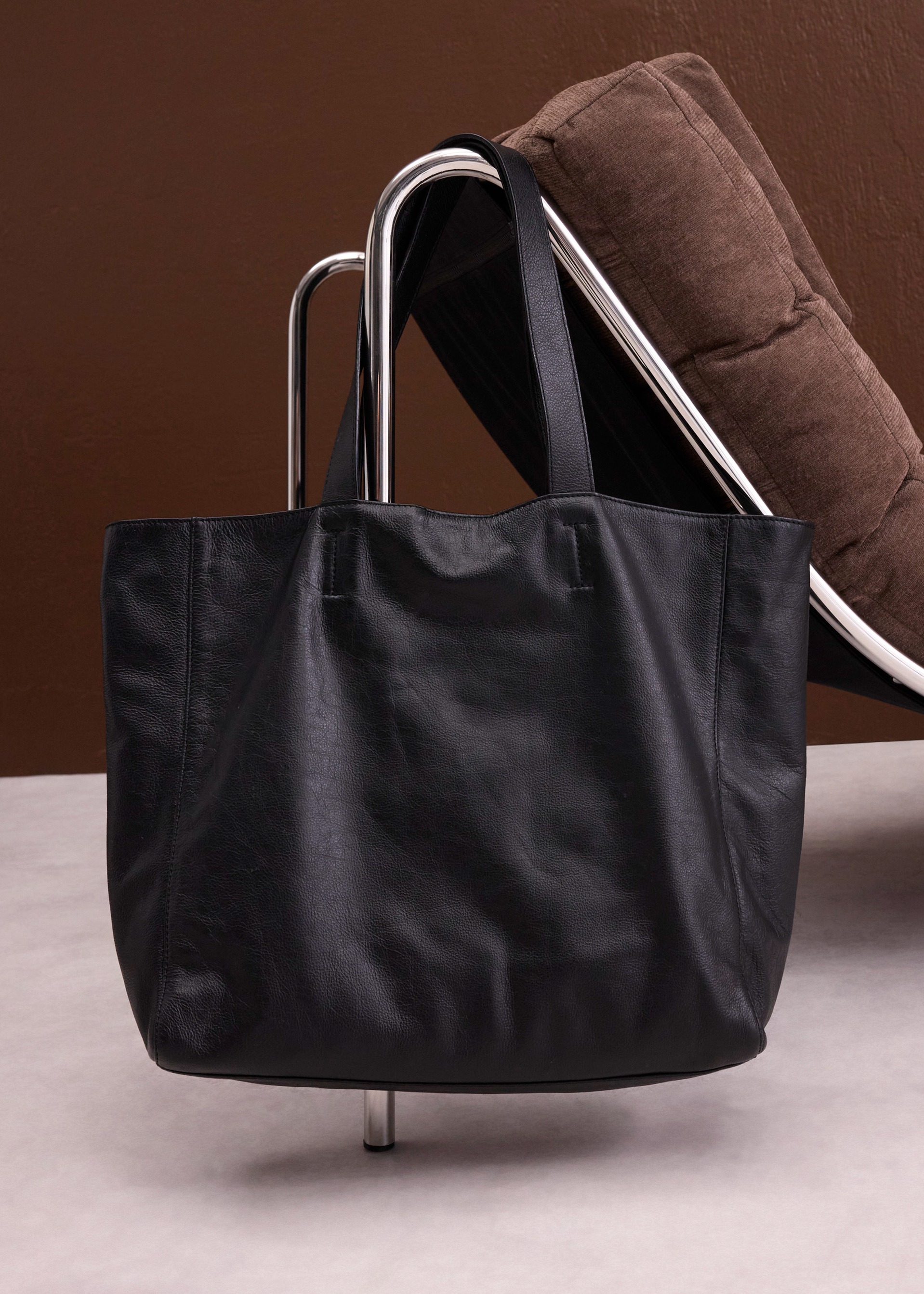 Diese geräumige schwarze Ledertasche hängt elegant an einem modernen Stuhl.