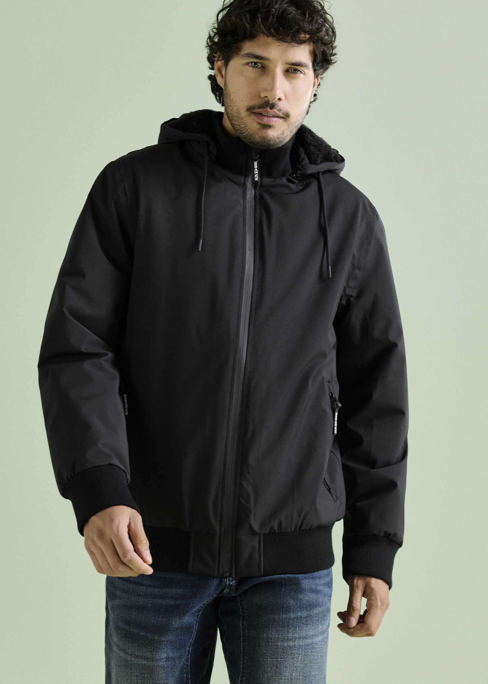 Man trägt eine schwarze Kapuzenjacke mit Reißverschluss und blaue Jeans.
