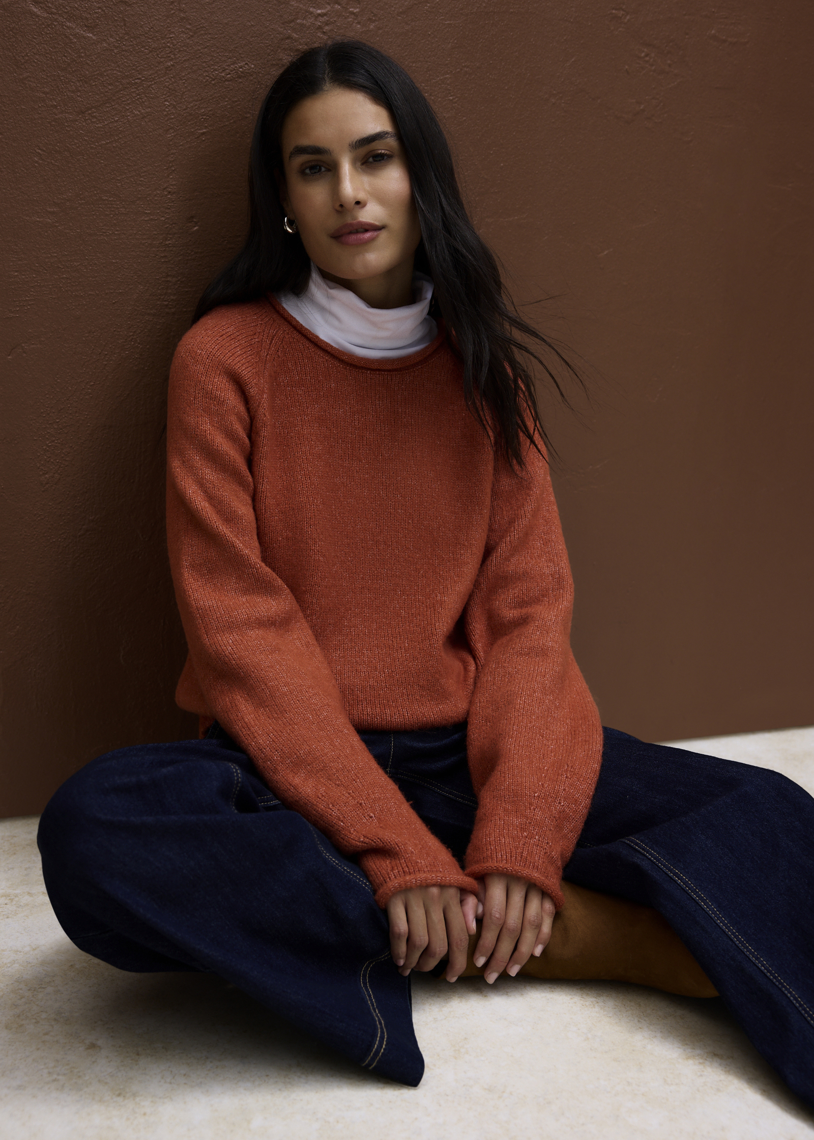 Orangefarbener Pullover über weißem Rollkragen und weite dunkle Jeans.
