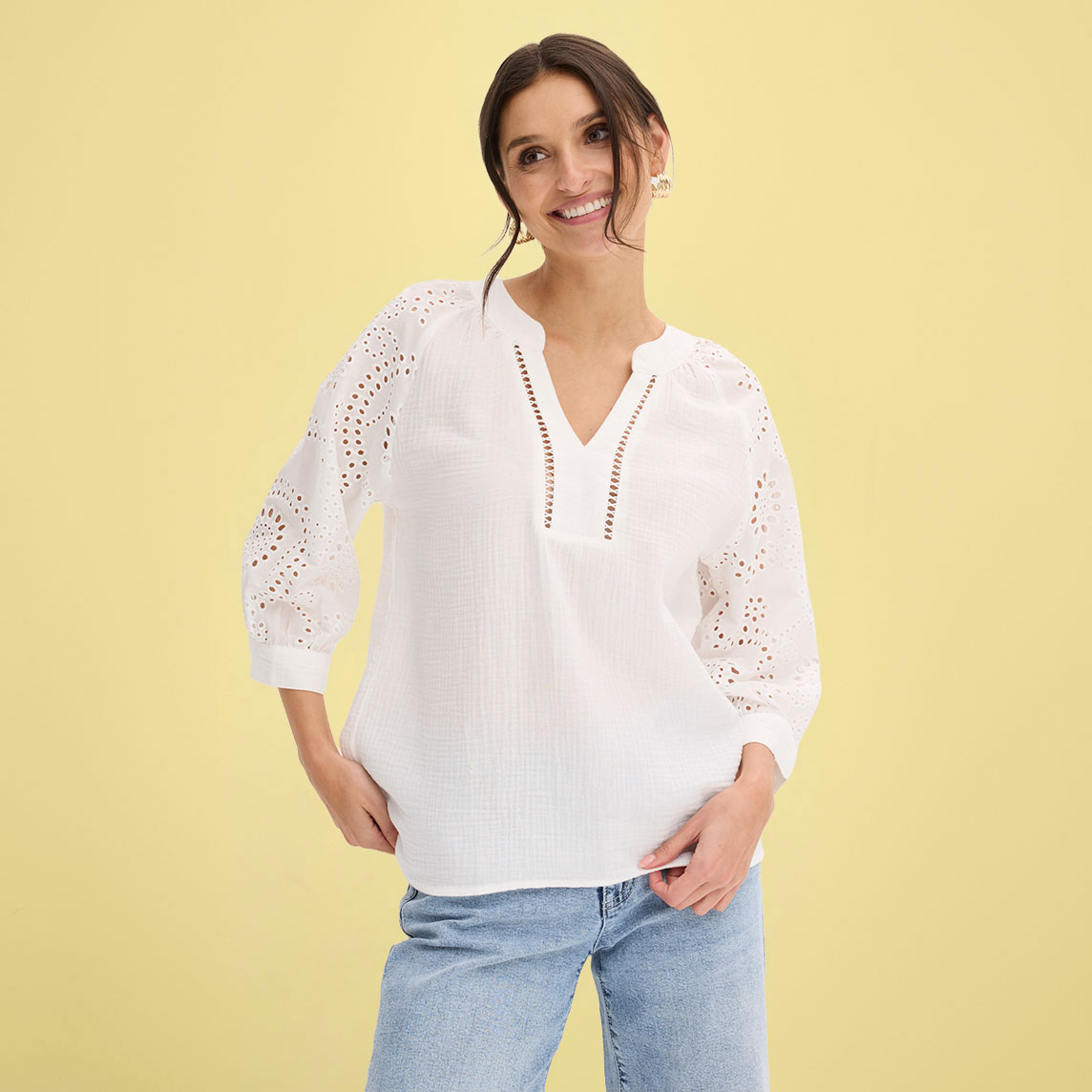 Weiße Bluse mit Lochstickerei und Dreiviertelärmeln, kombiniert mit lässiger Jeans.