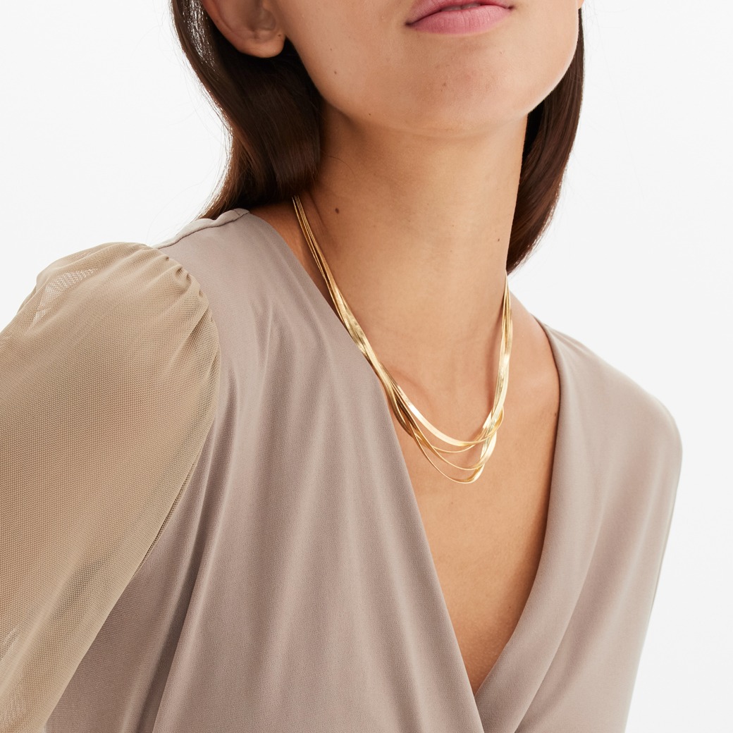 Elegantes Wickel-Oberteil mit transparenten Ärmeln, dazu goldene Halskette und Armband.