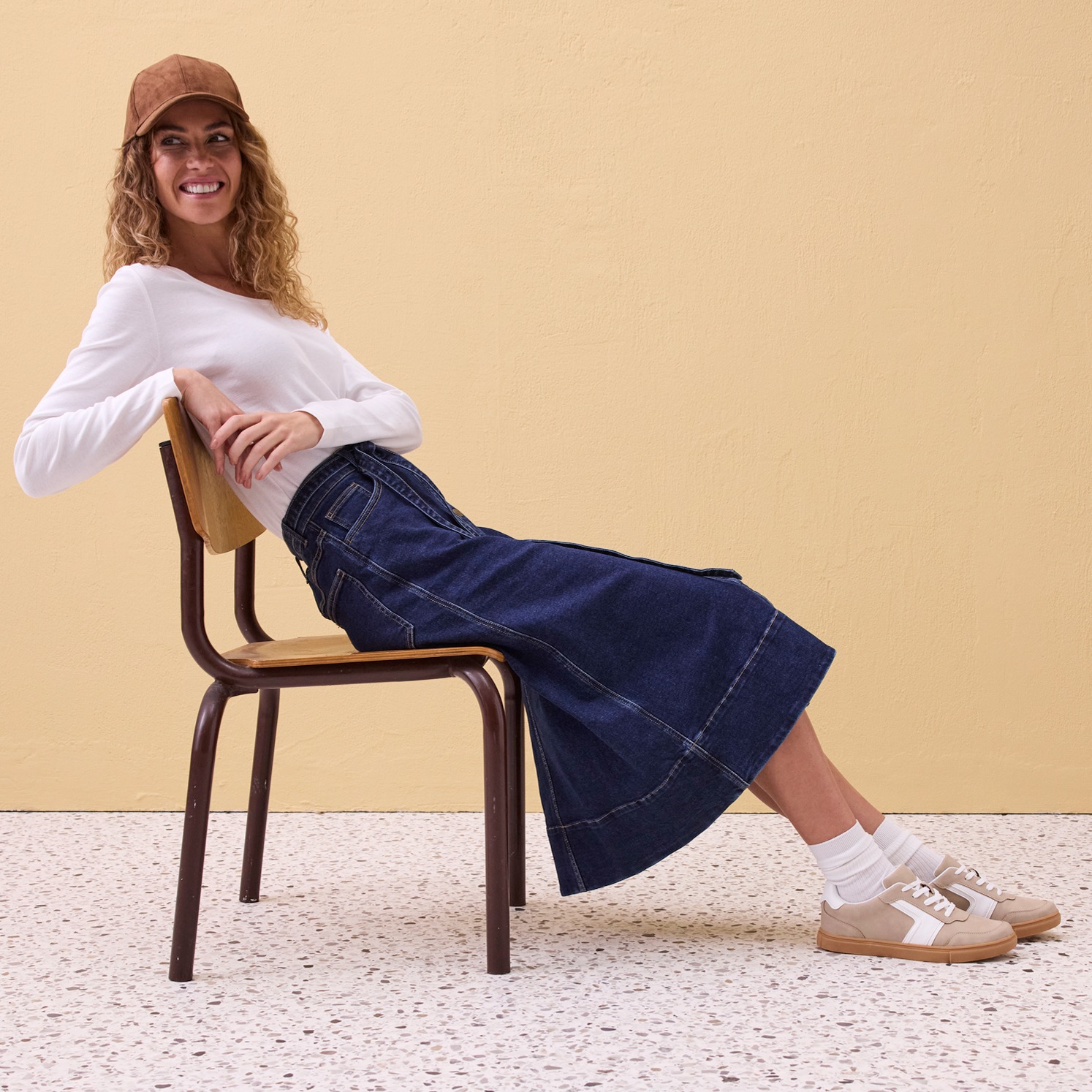 Weißes Langarmshirt, langer Jeansrock, Baseballmütze und bequeme weiße Sneaker.