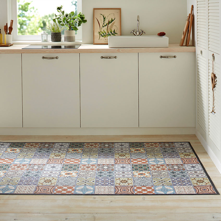 Bunter Teppich mit vielfältigen Mustern schmückt den Küchenboden vor schlichten, hellen Unterschränken.
