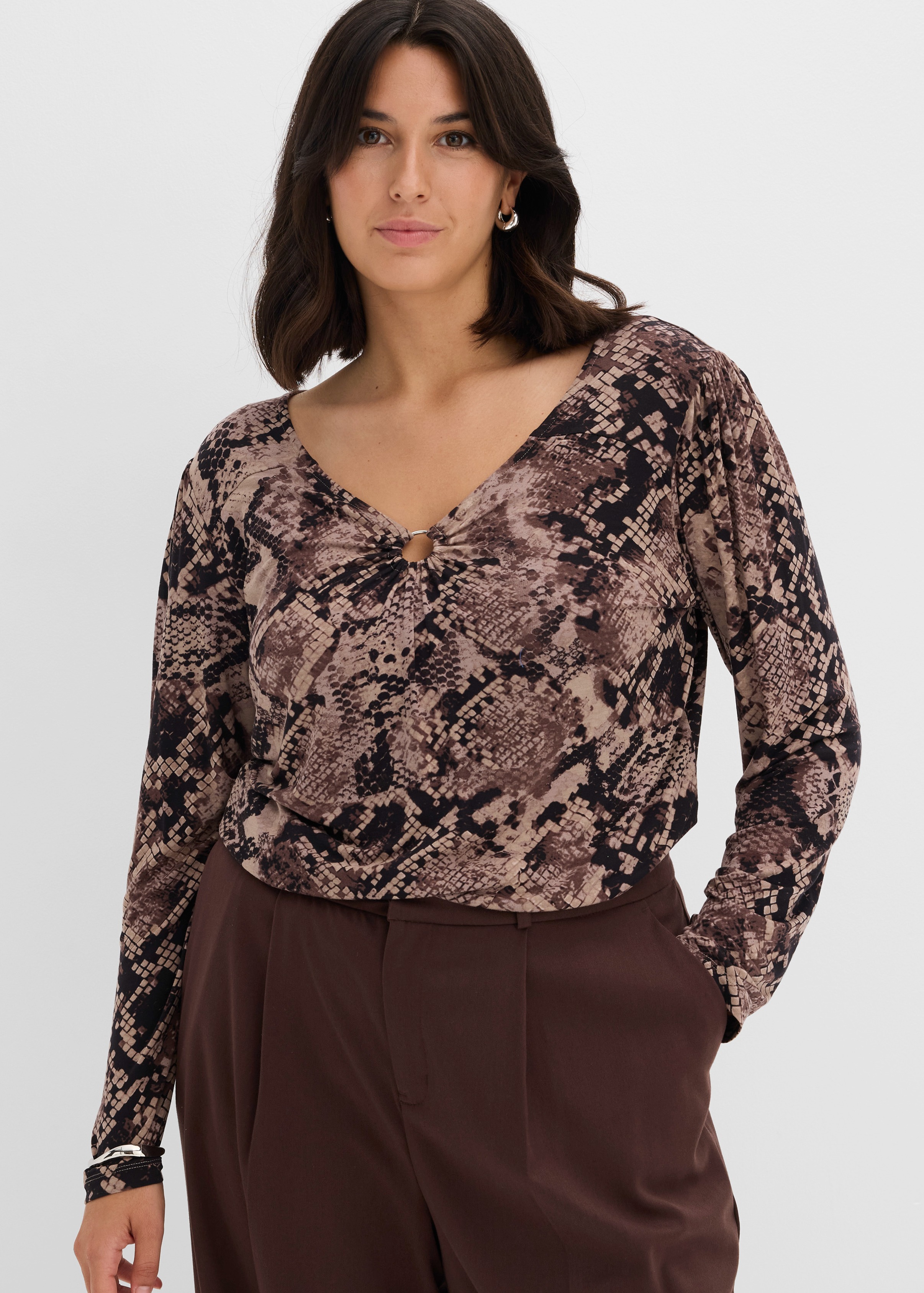 Modisches Schlangenmuster-Oberteil mit V-Ausschnitt und Ringdetail, kombiniert mit einer braunen Hose.