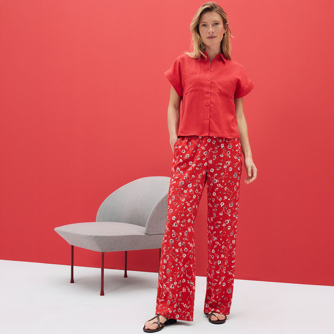 Rotes Kurzarm-Hemd und fließende Hose mit floralem Muster. Sommerliches Outfit vor leuchtend rotem Hintergrund.