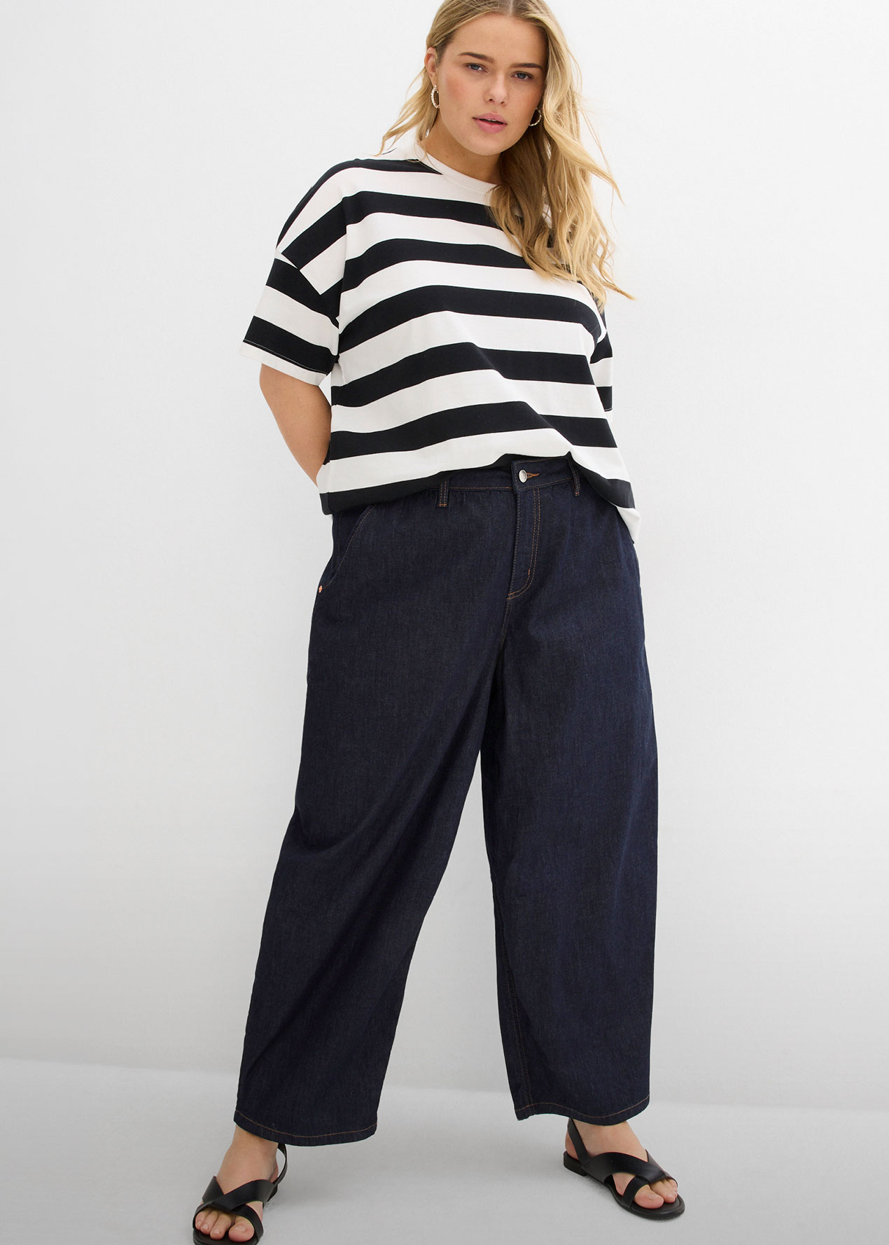 Gestreiftes Oberteil, weite dunkelblaue Jeans und schwarze Sandalen.