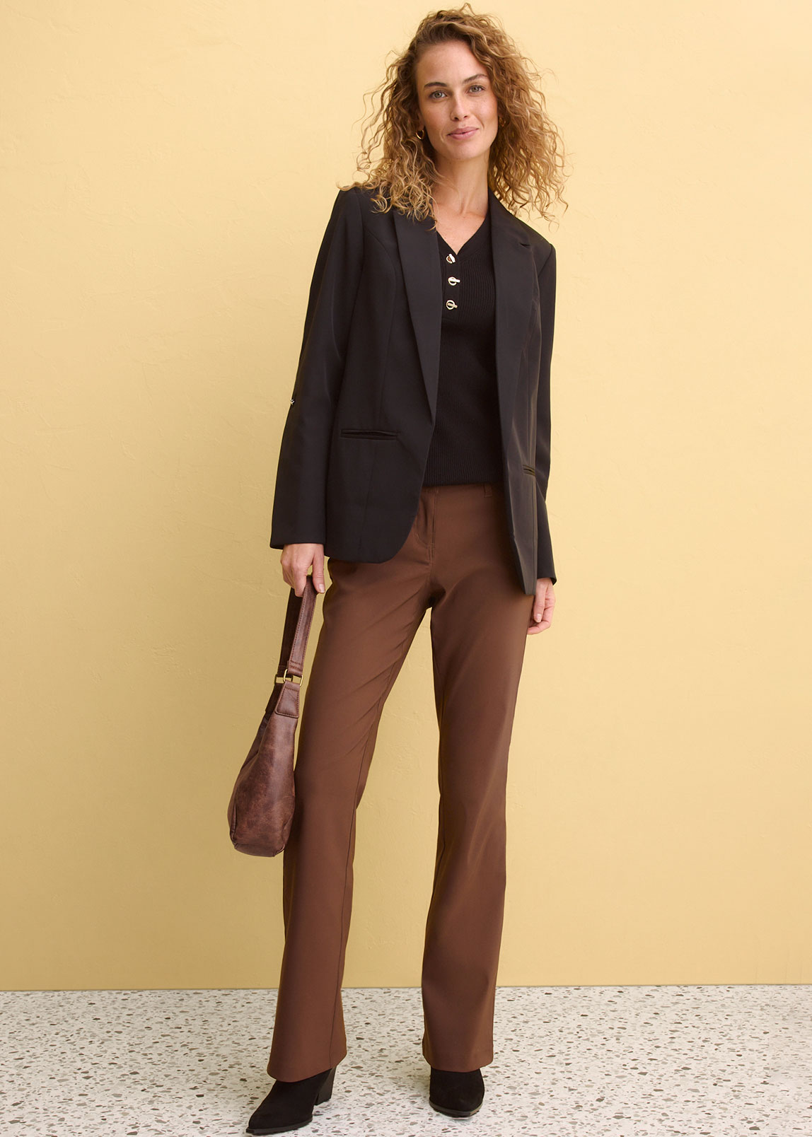 Schwarzer Blazer über dunklem Top, kombiniert mit brauner Hose.