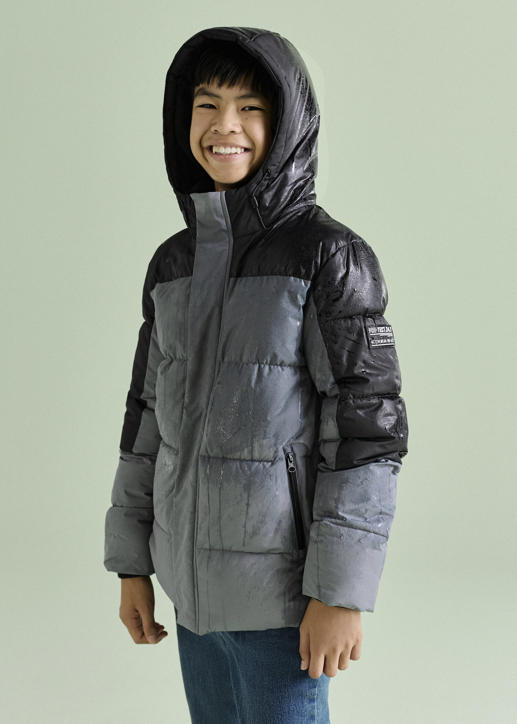 Der Junge trägt eine stylische zweifarbige Steppjacke mit Kapuze und Jeans.