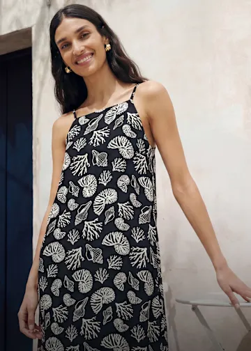 Frau in einem schwarzen Sommerkleid mit Muschel- und Korallenmuster.