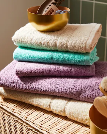 Flauschige, bunte Handtücher in Creme, Mint und Lila, ordentlich gestapelt.