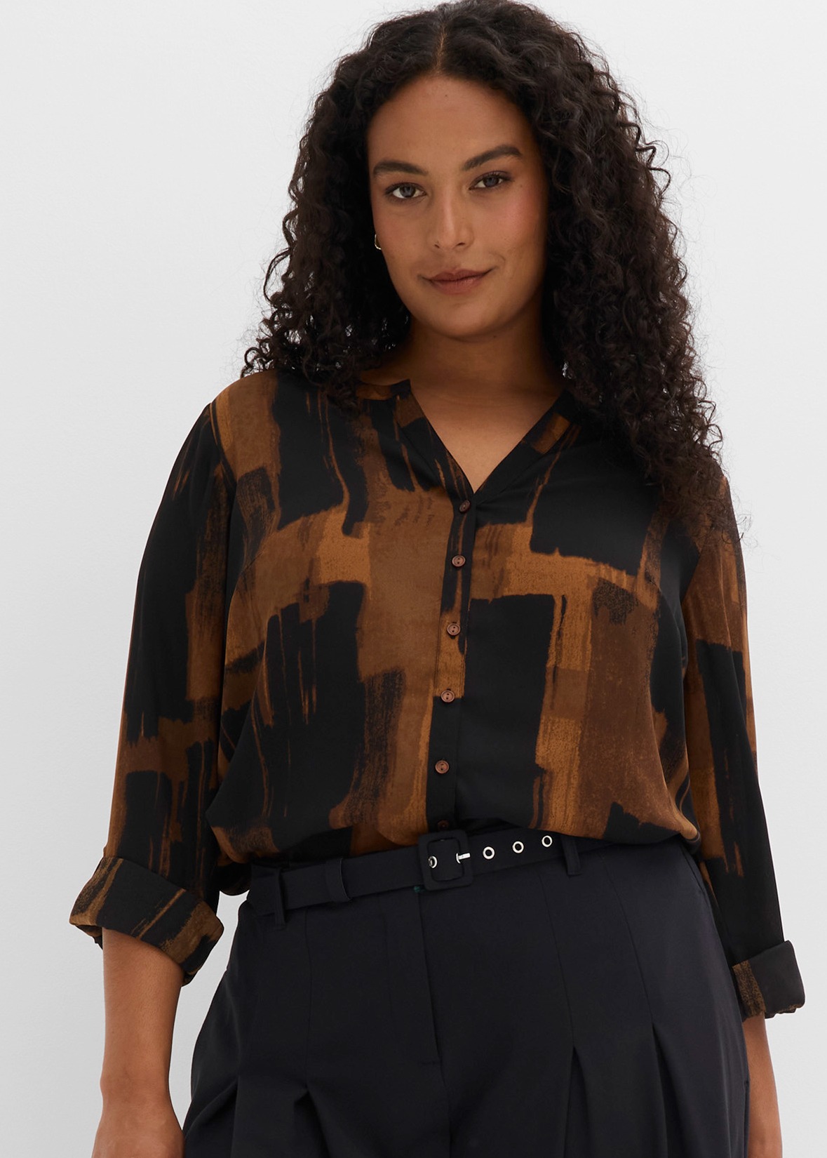 Modische Bluse in Braun und Schwarz mit dunkler Hose und stilvollem Gürtel.