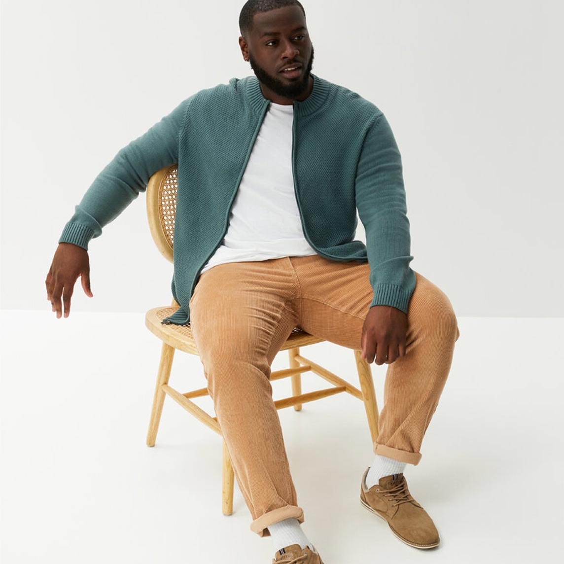 Grüne Strickjacke über weißem Shirt, beige Hose und braune Schuhe.